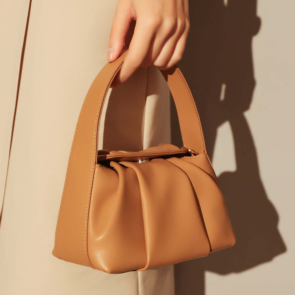 Ruched Leather Handbag held in hand, showcasing elegant pleats and a stylish silhouette.
